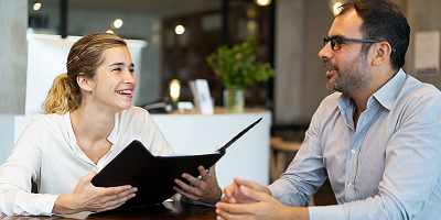 Female life insurance client sitting at table holding folder and talking to male life insurance agent