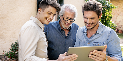 Older father and adult sons standing outside using tablet