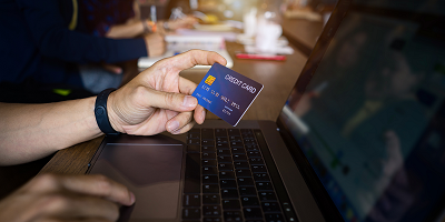 Man holding credit card and using laptop in cafe