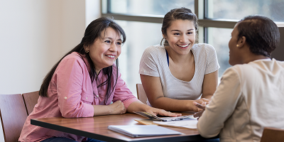 Mother and teenage daughter sitting at desk across from advisor
