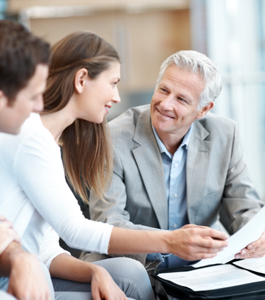 A mature financial advisor smiles as he assists a young couple with their financial planning. 