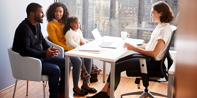 Black husband and wife with young daughter on her lap sitting at a desk across from female life insurance agent