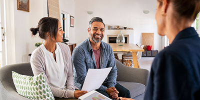 Husband and wife sitting on couch across from female life insurance agent