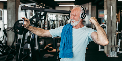 Older man flexing bicep and taking a selfie at the gym