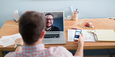 Man using smartphone during a video conference on laptop