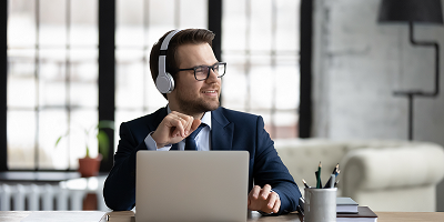 Financial professional with glasses wearing headphones in front of open laptop