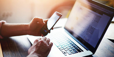 Man holding smartphone and using laptop