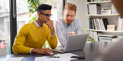 Two male coworkers sitting next to each other and discussing business over a laptop
