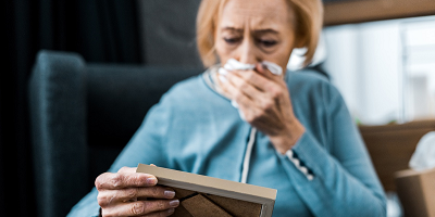 A senior woman crying as she looks at a picture frame. 