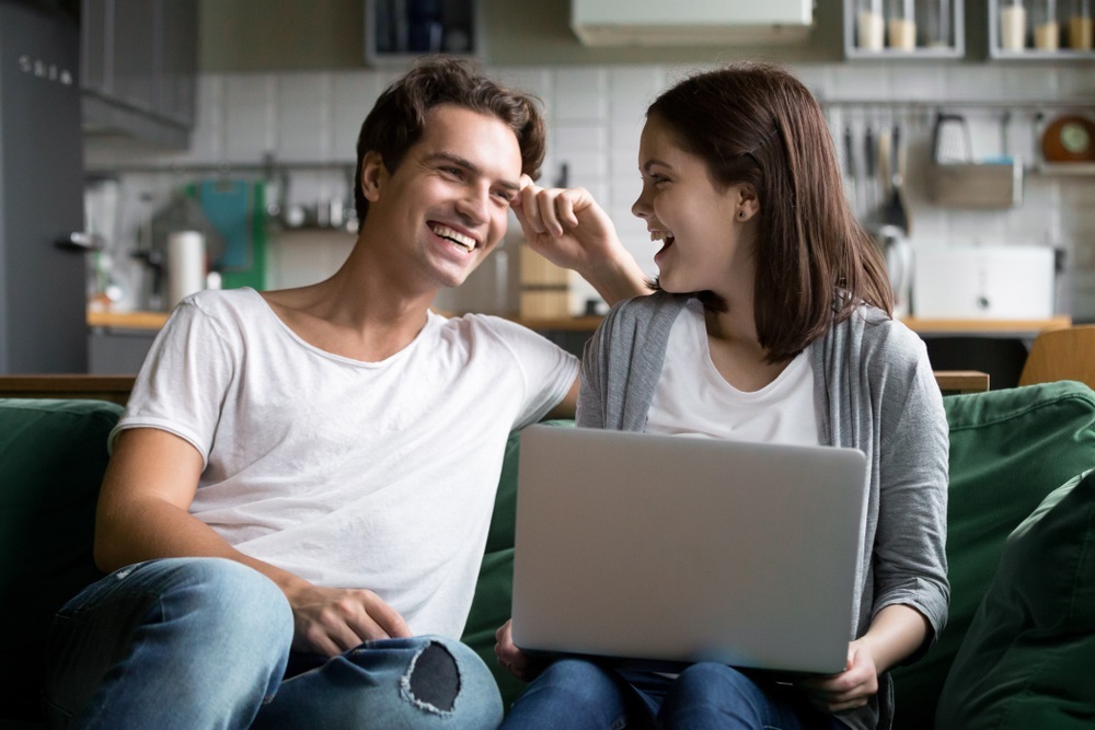 Millennial couple sitting on couch reviewing their finances on laptop.