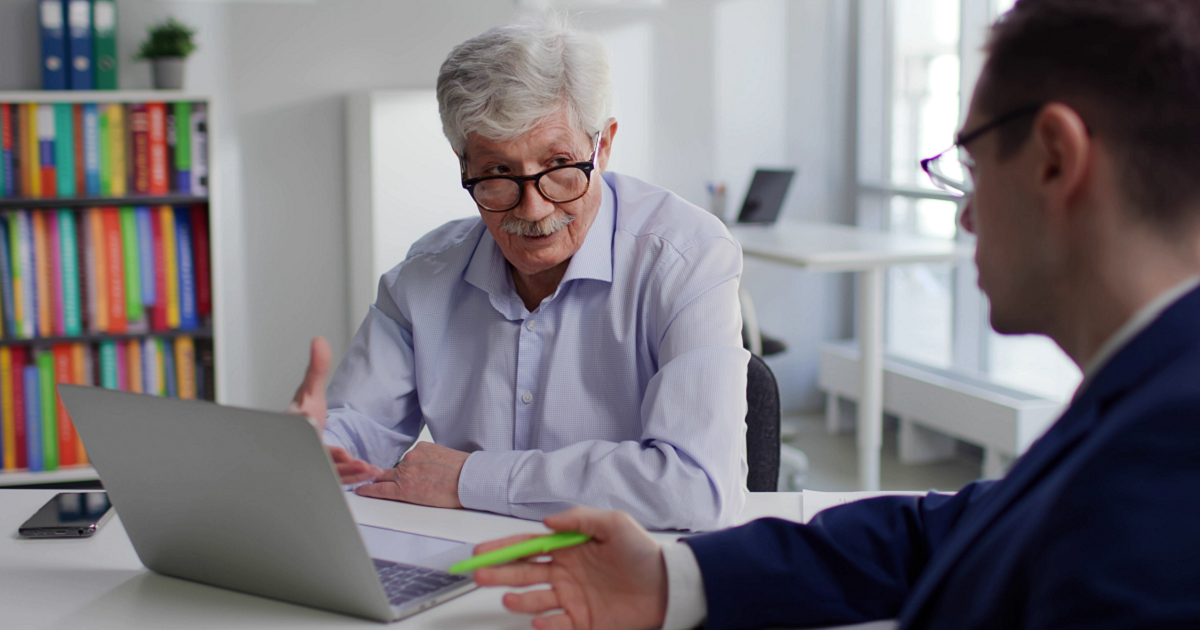 Older man sitting at table with laptop talking to financial advisor