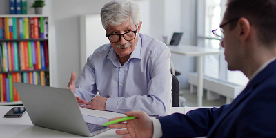 Older man sitting at table with laptop talking to financial advisor
