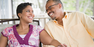 Mature African-American couple smiling as they sit in their rocking chairs on a front porch. 