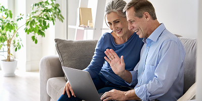 Older couple sitting on a couch talking to financial professional on a laptop